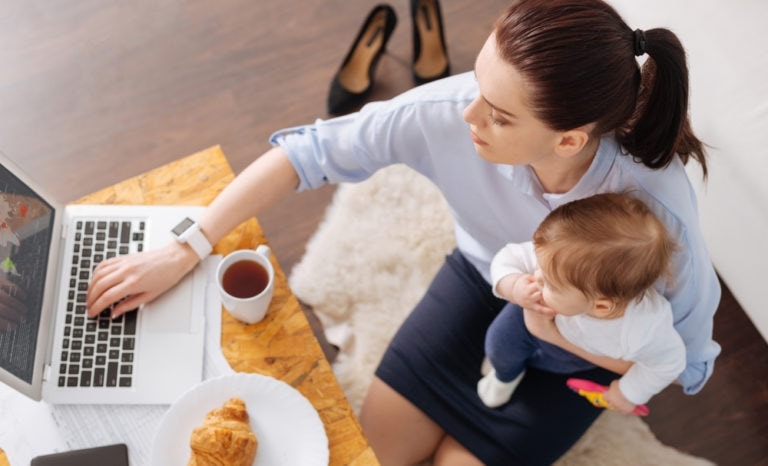 Mother working at a laptop while holding her child